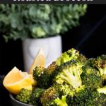 Roasted broccoli with lemon wedge garnish in a dark bowl.