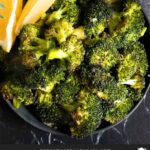 Roasted broccoli with lemon wedge garnish in a dark bowl.