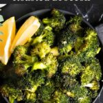 Roasted broccoli with lemon wedge garnish in a dark bowl.