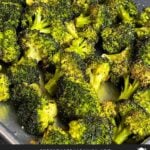Roasted broccoli with lemon wedge garnish in a dark bowl.