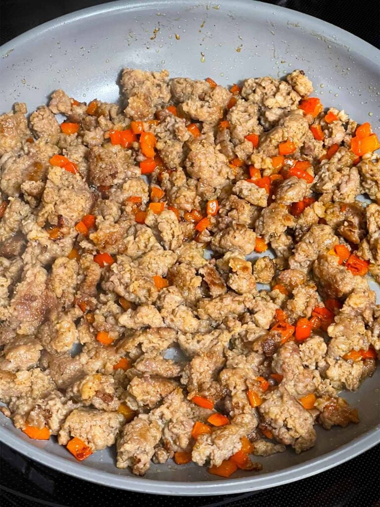 Browned sausage with diced red bell pepper in a skillet.