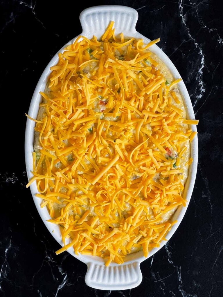 Sausage and cheese grits in a casserole dish, topped with shredded cheddar cheese.