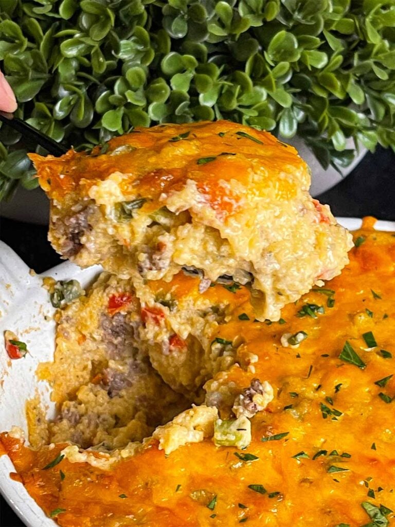 Baked sausage and cheese grits in a casserole dish with a serving resting on a spatula.