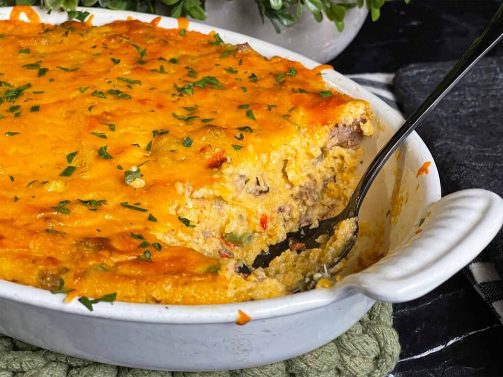 Baked sausage and cheese grits in a casserole dish with a serving cut out.