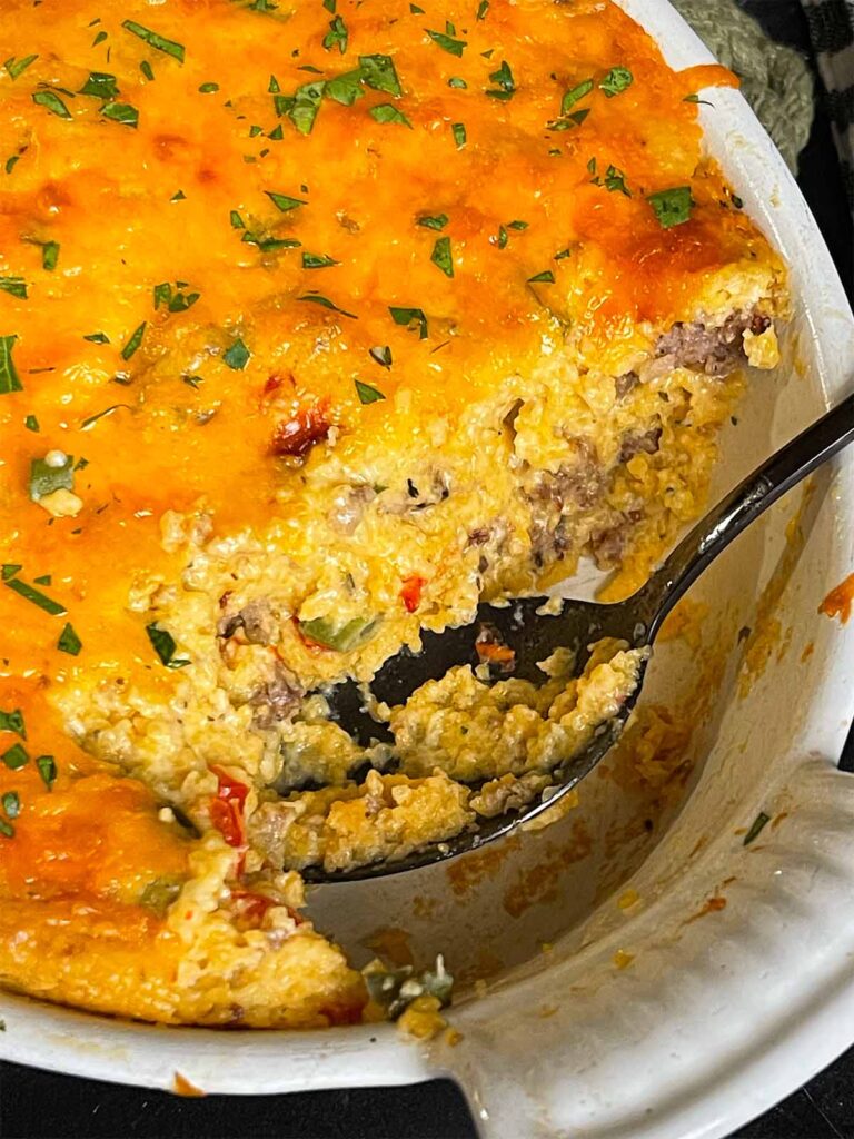 Baked sausage and cheese grits in a casserole dish with a serving cut out.