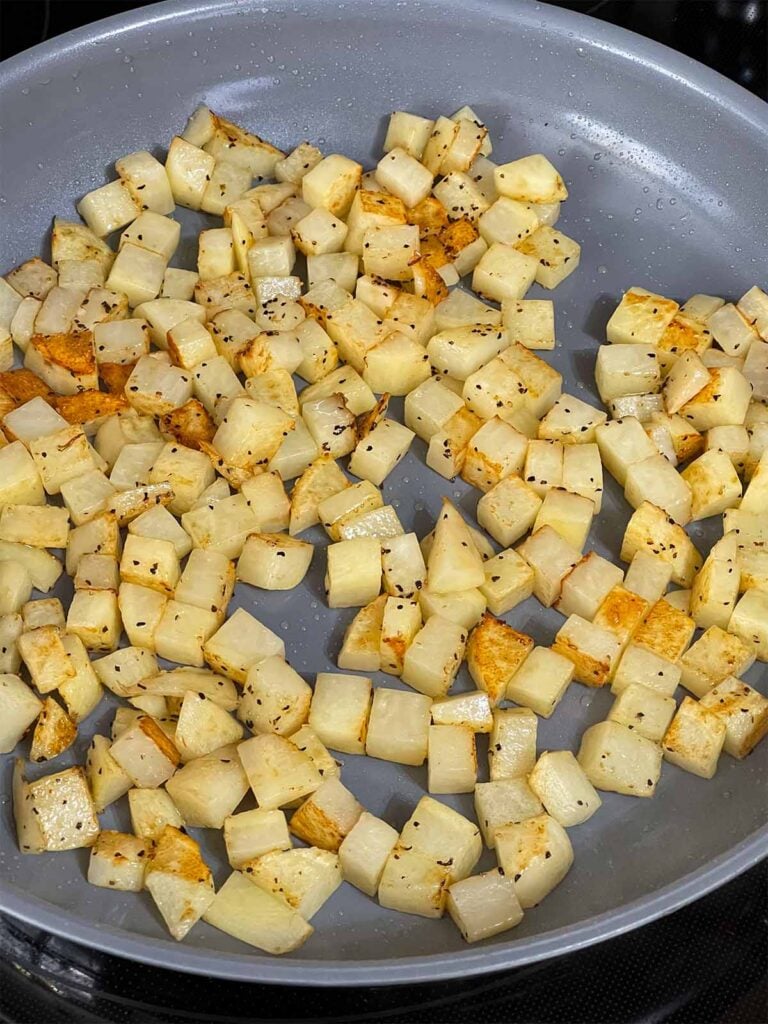 Browning diced and seasoned potatoes in a skillet.