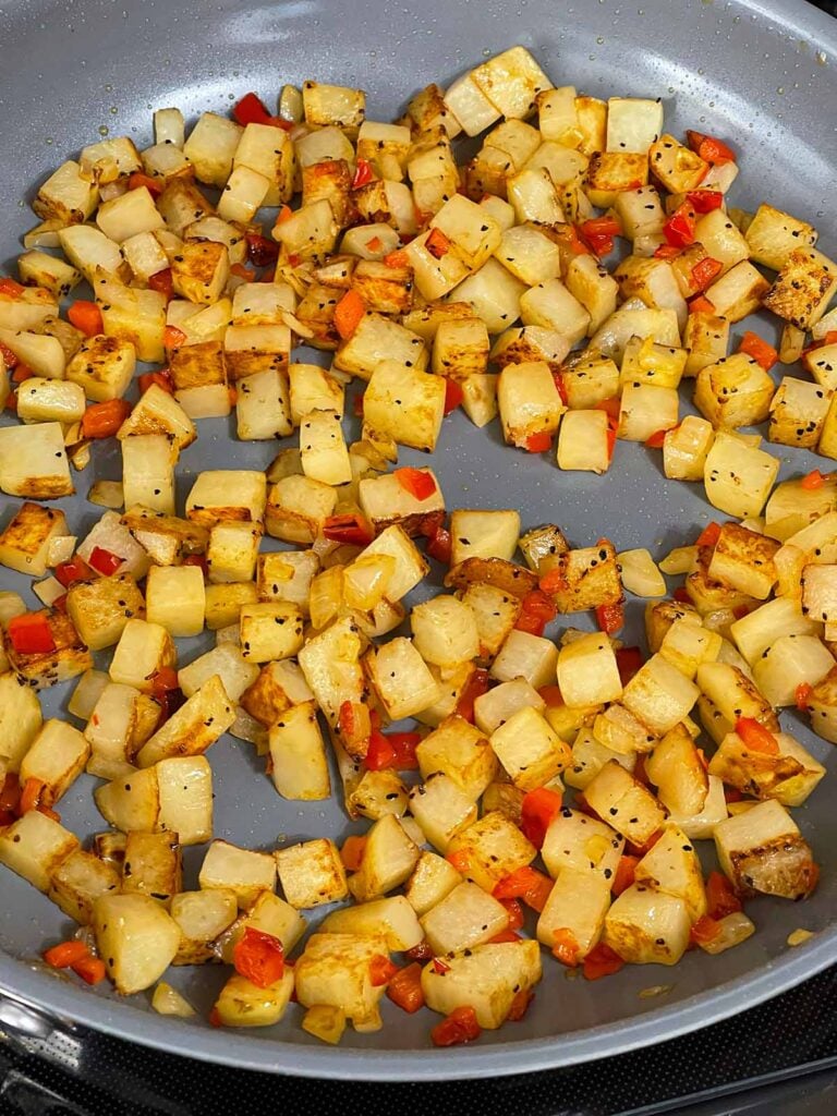 Potatoes, onion, and red bell pepper cooking in a skillet.