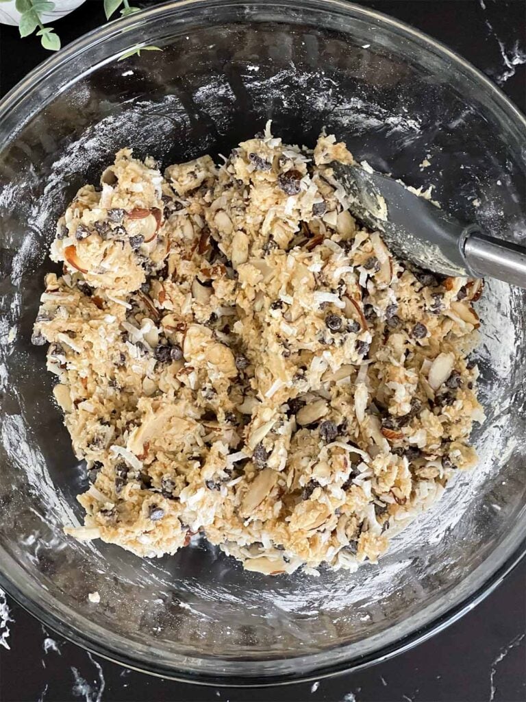 Almond joy cookie dough batter with the almonds, coconut flakes, and mini semi sweet chocolate chips added in a glass mixing bowl.