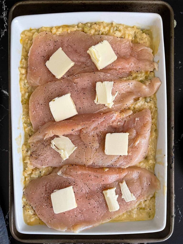 Chicken breast halves topped with pat of butter on top of the rice mixture.