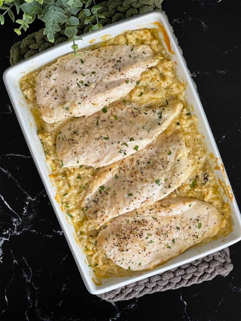Chicken and rice casserole garnished with chopped parsley in a light baking pan on a dark surface.