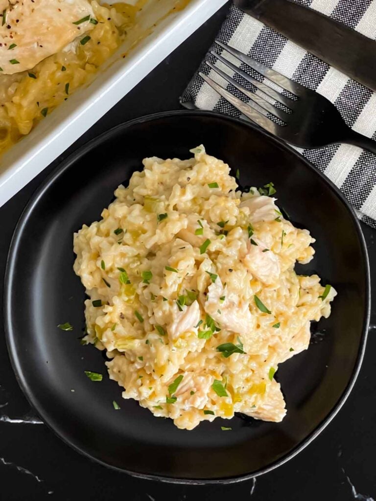 Chicken and rice casserole garnished with chopped parsley on a dark plate on a dark surface.