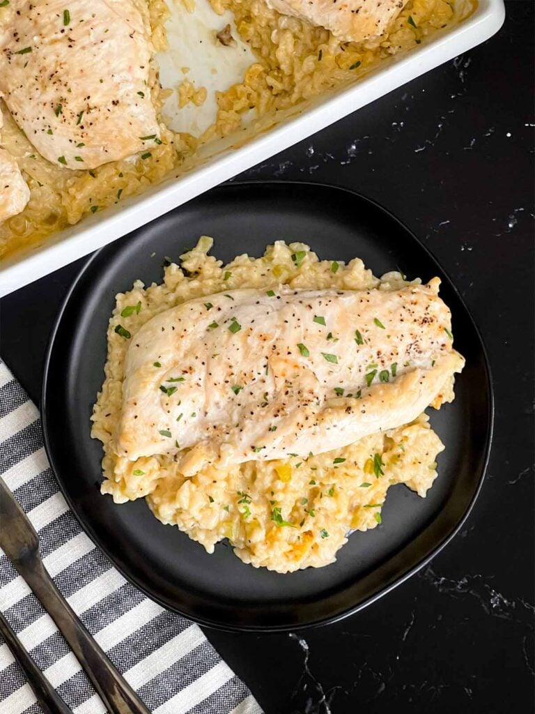 Chicken and rice casserole garnished with chopped parsley on a dark plate on a dark surface.