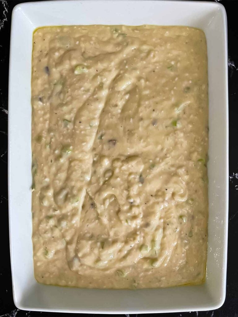 Soup and rice mixture for chicken and rice casserole in a light baking pan on a dark surface.