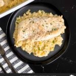 Chicken and rice casserole garnished with chopped parsley on a dark plate on a dark surface.