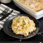 Chicken and rice casserole garnished with chopped parsley on a dark plate on a dark surface.