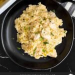 Chicken and rice casserole garnished with chopped parsley on a dark plate on a dark surface.