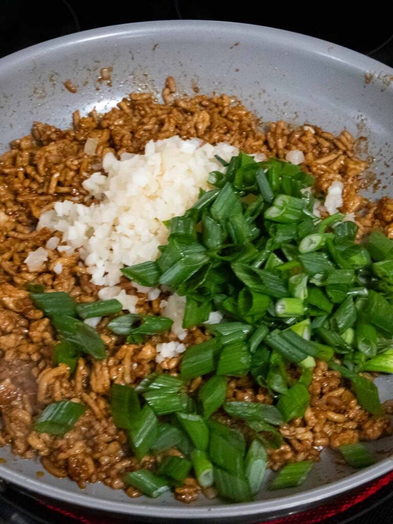 Green onions and water chestnuts added to seasoned ground chicken in a skillet.