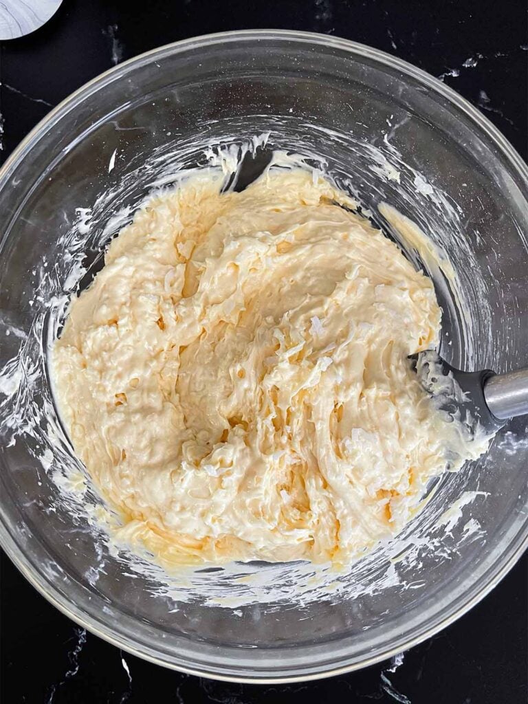 Coconut sheet cake batter in a glass mixing bowl on a dark surface.