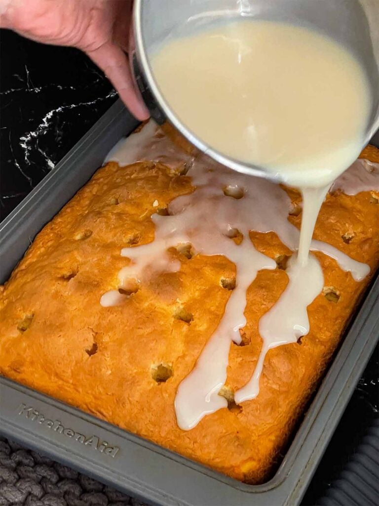 Cream of coconut mixture being poured over the coconut sheet cake still hot in the baking pan.