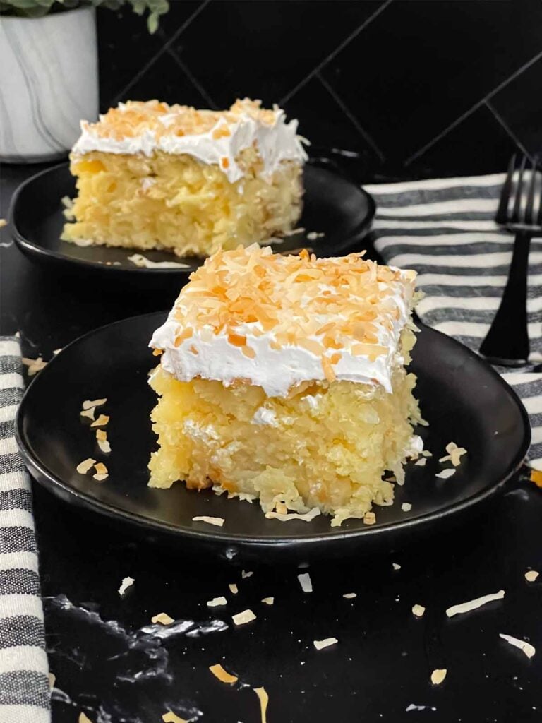 Coconut sheet cake slice on a dark plate on a dark surface.