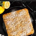 Lemon crumb cake dusted with powdered sugar on a dark plate on a dark surface.