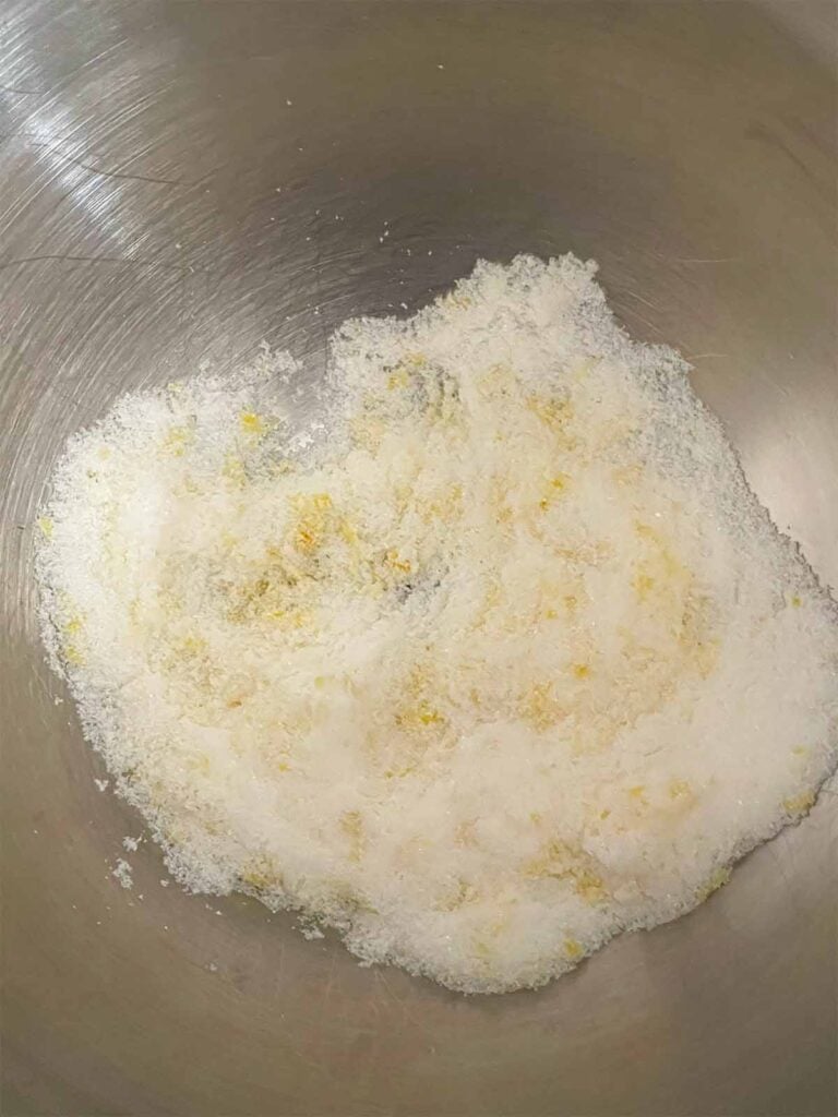 Granulated sugar and lemon zest rubbed together in a metal mixing bowl.