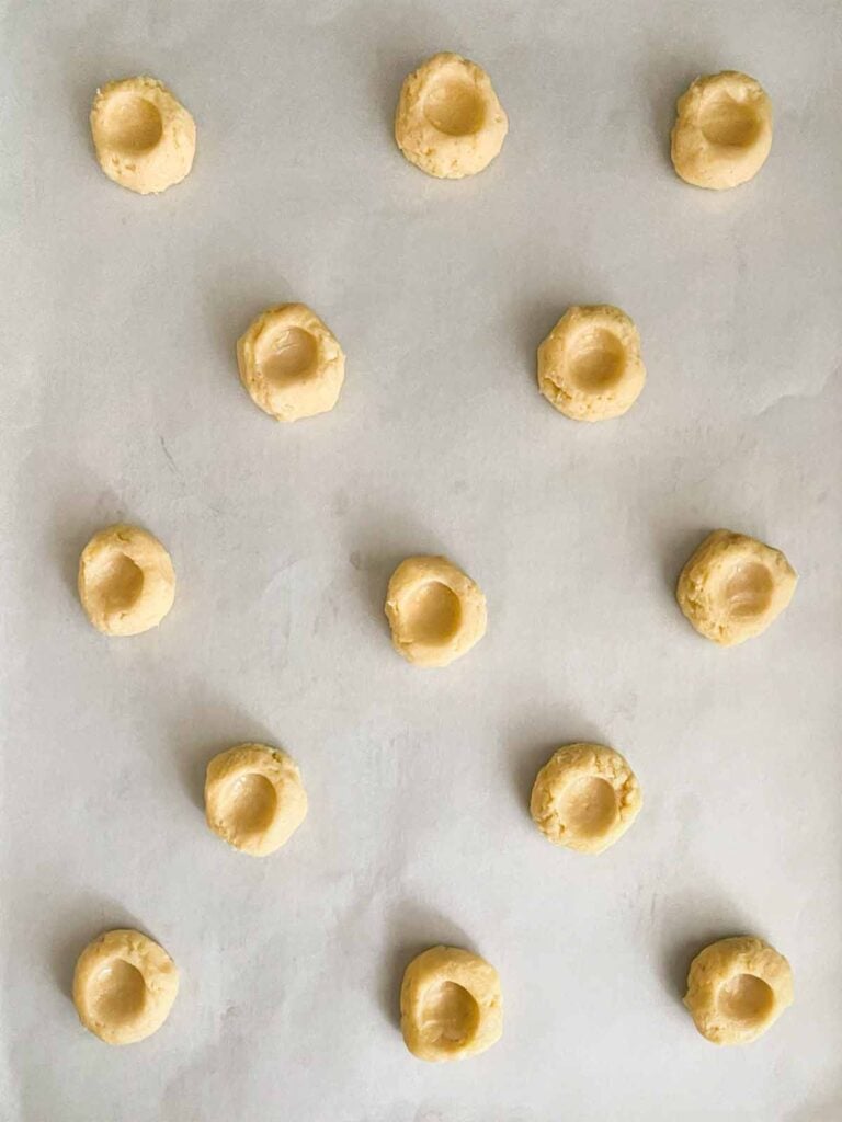 Lemon thumbprint cookie dough with thumb indentations formed on parchment paper lined baking sheet.