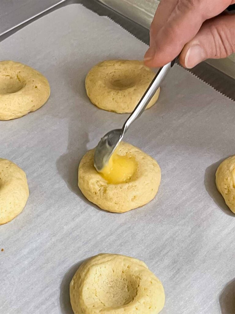 Lemon curb being placed in the thumbprint of the cookies.