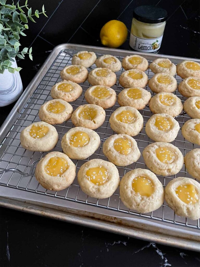 Lemon thumbprint cookies on a wire rack on a dark surface.