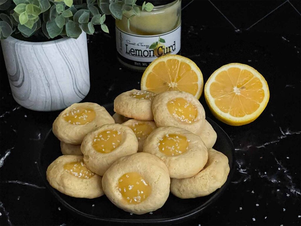 Lemon thumbprint cookies on a dark plate on a dark surface.