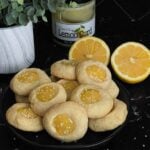 Lemon thumbprint cookies on a dark plate on a dark surface.