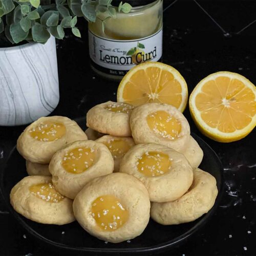 Lemon thumbprint cookies on a dark plate on a dark surface.