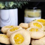 Lemon thumbprint cookies on a dark plate on a dark surface.