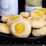 Lemon thumbprint cookies on a dark plate on a dark surface.