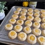 Lemon thumbprint cookies on a wire rack on a dark surface.