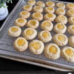 Lemon thumbprint cookies on a wire rack on a dark surface.