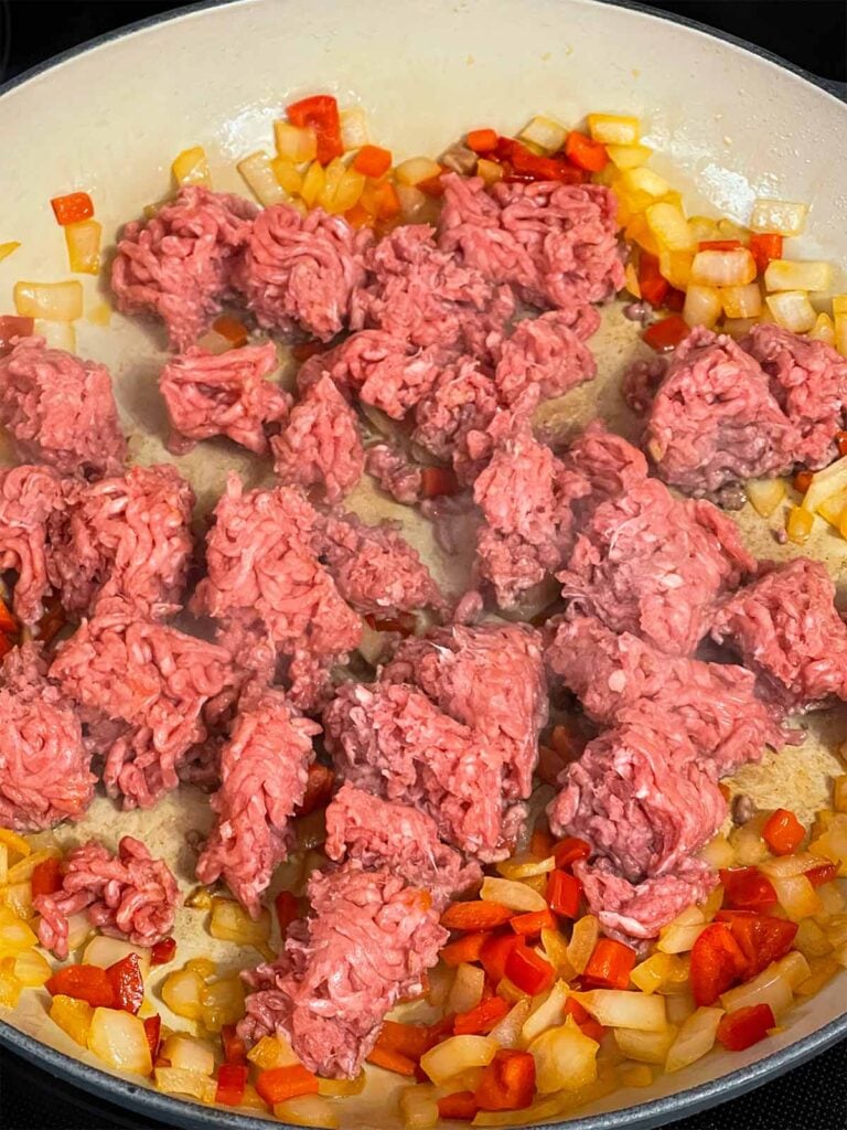 Ground beef added to onions and red bell pepper in a skillet.
