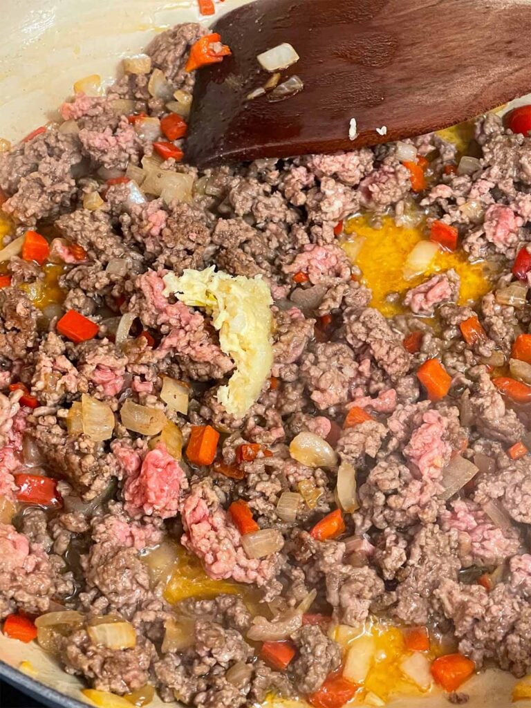 Adding garlic to ground beef, red bell peppers, and onion in a skillet.