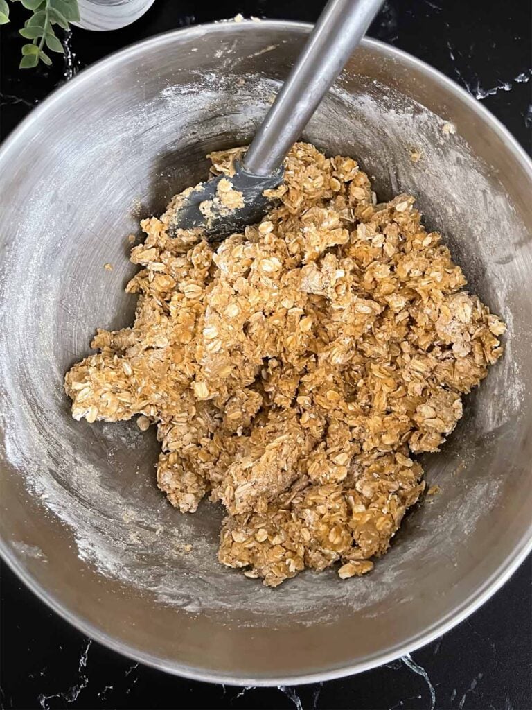 Oatmeal cookie dough for oatmeal fudge bars mixed in a metal mixing bowl.