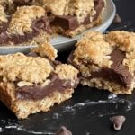 Oatmeal fudge bars on a dark surface in front of a plate of more bars.