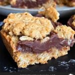 Oatmeal fudge bars on a dark surface in front of a plate of more bars.