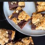 Oatmeal fudge bars on a dark surface in front of a plate of more bars.