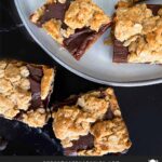 Oatmeal fudge bars on a dark surface in front of a plate of more bars.