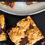 Oatmeal fudge bars on a dark surface in front of a plate of more bars.