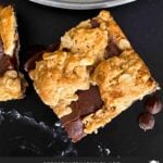 Oatmeal fudge bars on a dark surface in front of a plate of more bars.