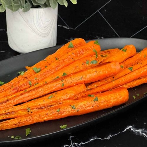 Roasted whole carrots on a dark plate garnished with chopped parsley.