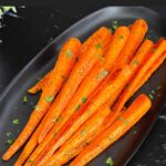 Roasted whole carrots on a dark plate garnished with chopped parsley.