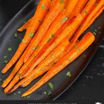 Roasted whole carrots on a dark plate garnished with chopped parsley.