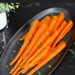 Roasted whole carrots on a dark plate garnished with chopped parsley.