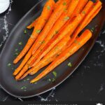 Roasted whole carrots on a dark plate garnished with chopped parsley.